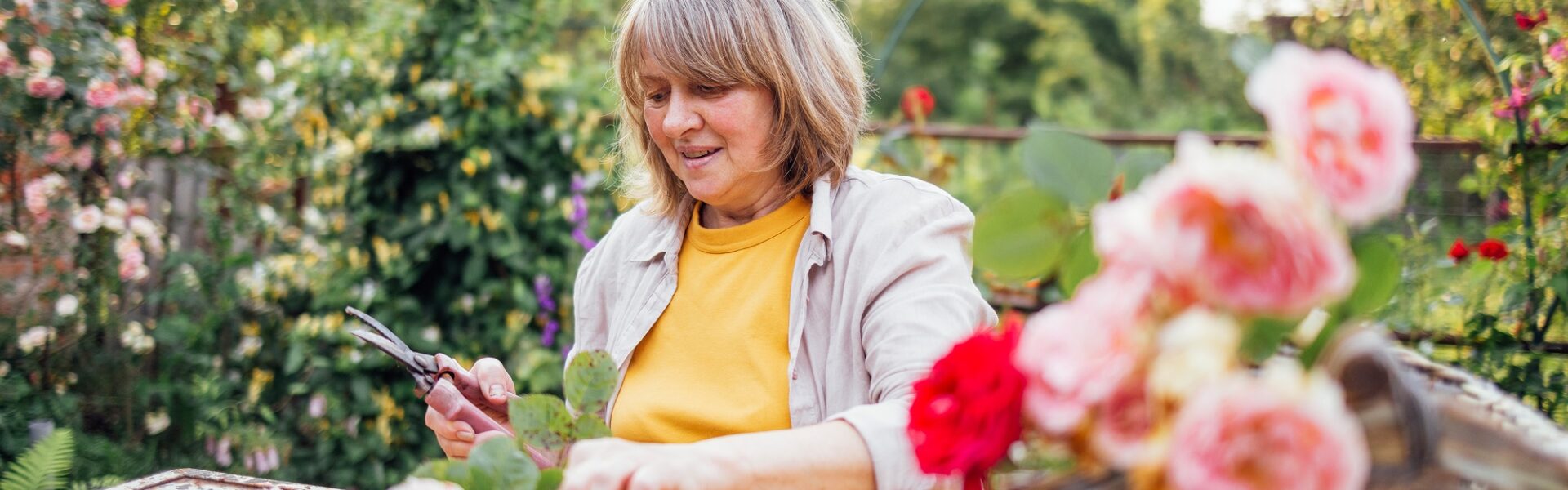 A middle-aged woman is sitting at a table and picking a bouquet of roses outdoors