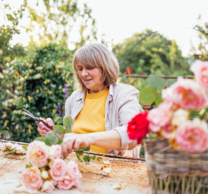 A middle-aged woman is sitting at a table and picking a bouquet of roses outdoors