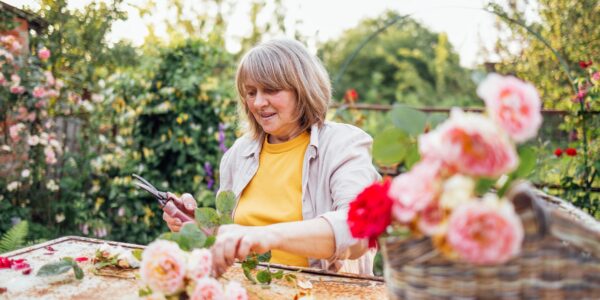 A middle-aged woman is sitting at a table and picking a bouquet of roses outdoors