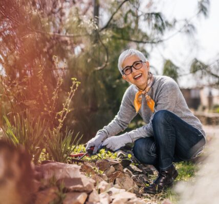 Cheerful retired woman prune shrubs and pulling the weeds in the garden.