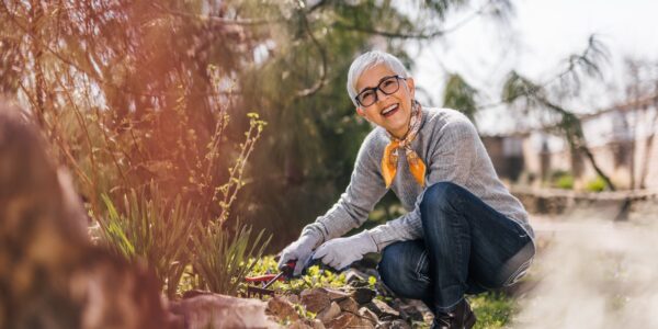 Cheerful retired woman prune shrubs and pulling the weeds in the garden.