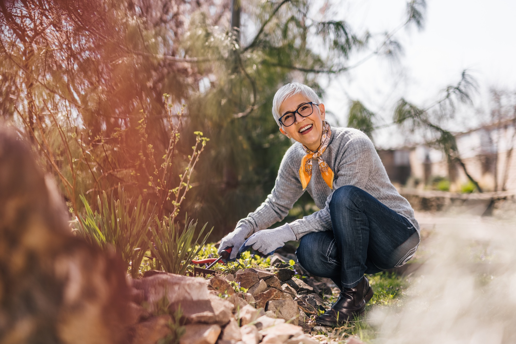 Cheerful retired woman prune shrubs and pulling the weeds in the garden.
