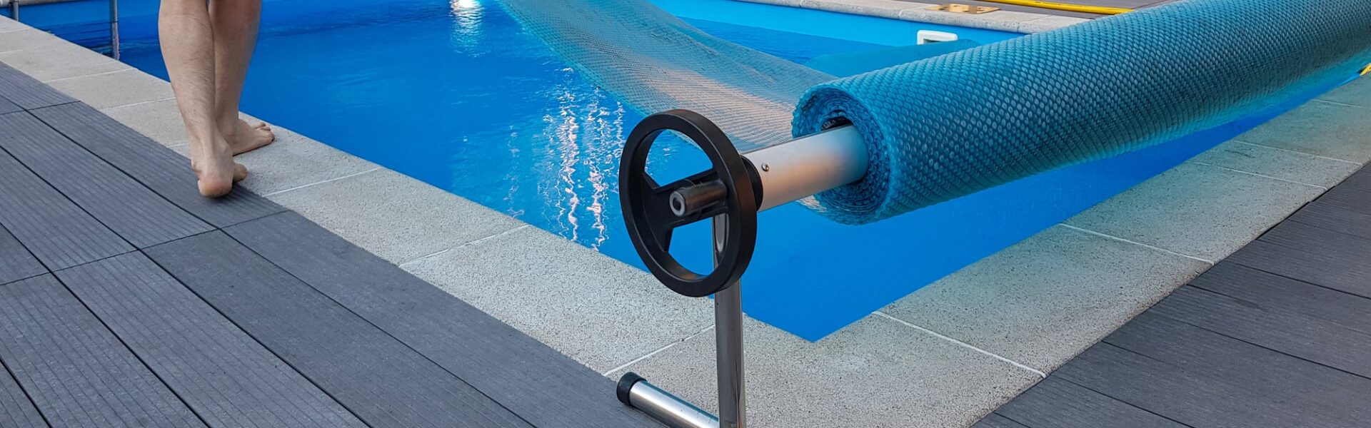 Man covers swimming pool with cover for protection against dirt, leaves, heating and cooling water.