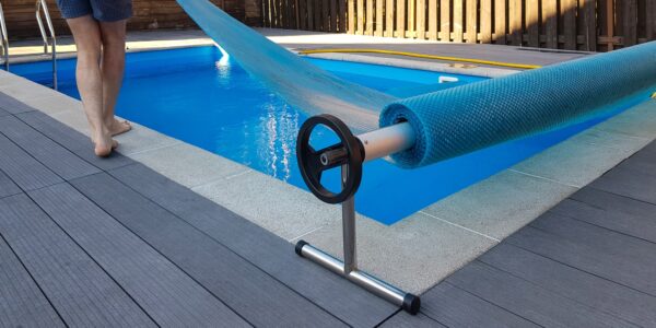 Man covers swimming pool with cover for protection against dirt, leaves, heating and cooling water.