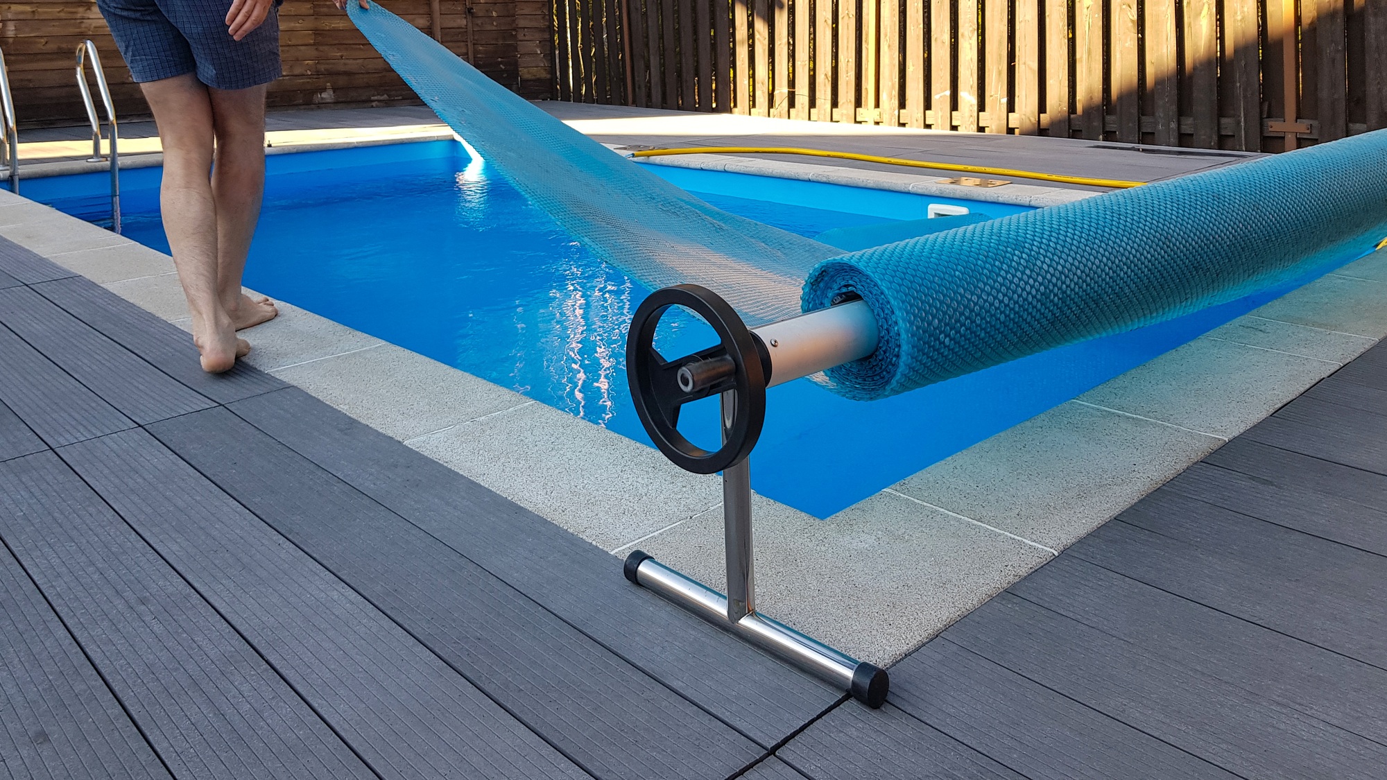 Man covers swimming pool with cover for protection against dirt, leaves, heating and cooling water.