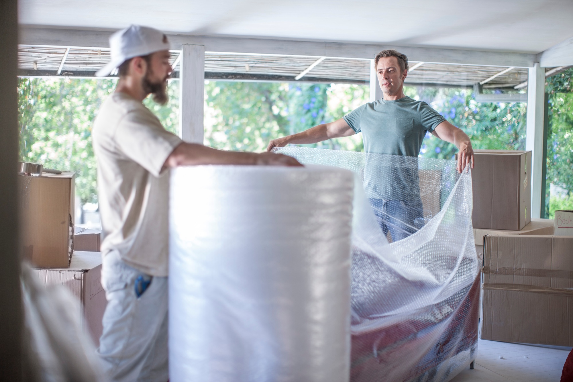 Moving house: two men unrolling bubble wrap in preparation for packing
