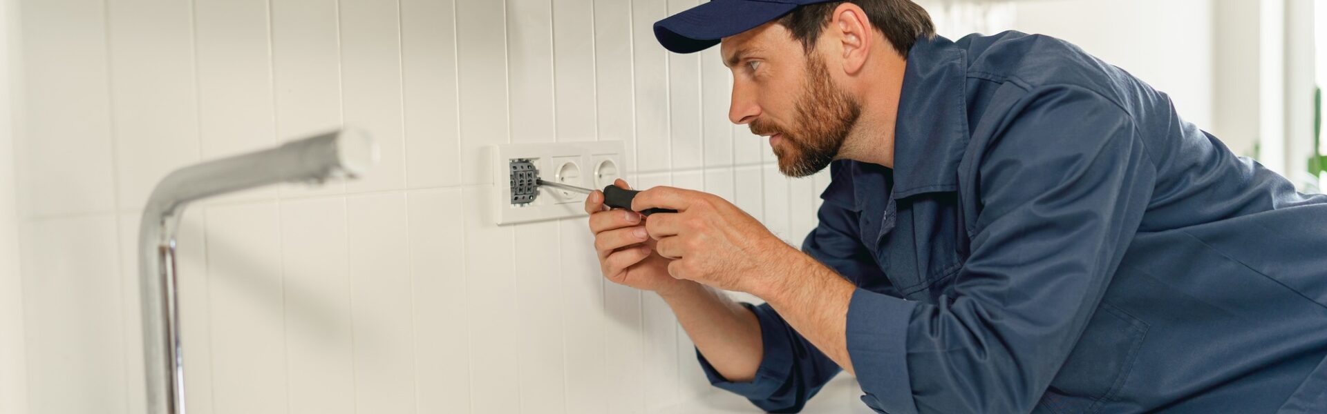 Professional handyman in uniform is fixing the electricity power socket on home kitchen