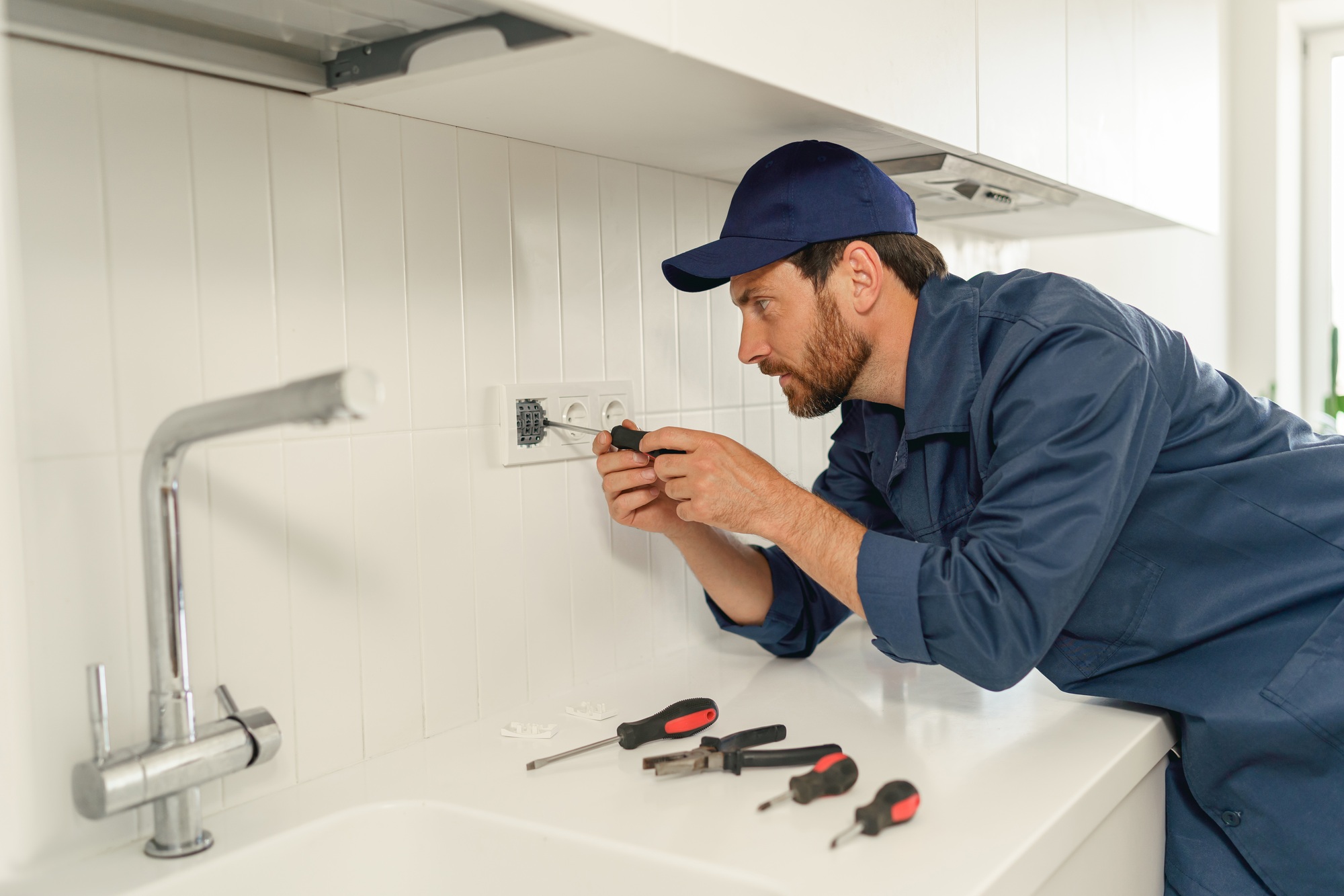 Professional handyman in uniform is fixing the electricity power socket on home kitchen